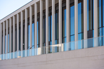 A modern building with vertical concrete struts and a continuous glass front. The clean lines and reflections create a minimalist aesthetic.