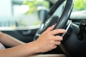 A car driver is holding and controlling on steering wheel of the modern car with digital display as background, close-up and selective focus a person hand. Transportation with people in action scene.