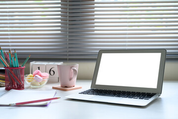 Chic feminine workspace with laptop, pastel decor, and soft lighting through window blinds