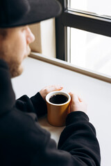Man with hands clasped near yellow mug of filter coffee on bright tabletop.