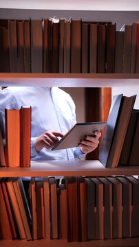 vertical video Man using tablet between bookshelves in library at night