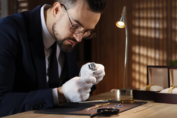 Appraiser with loupe evaluating ring at table indoors