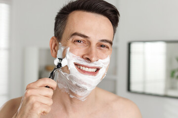 Smiling man shaving with razor at home