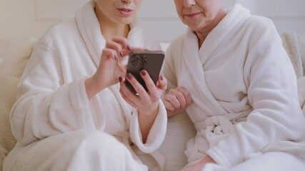 Senior lady and her daughter booking vacation on phone while relaxing in spa