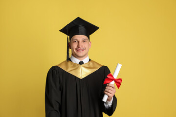 Happy student with diploma after graduation on yellow background