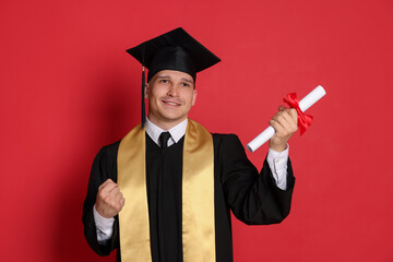 Happy student with diploma after graduation on red background