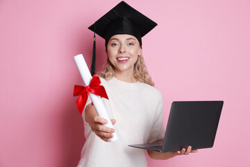 Happy student with diploma and laptop after graduation on pink background