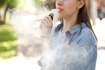Young woman using electronic smoking device outdoors, closeup. Space for text