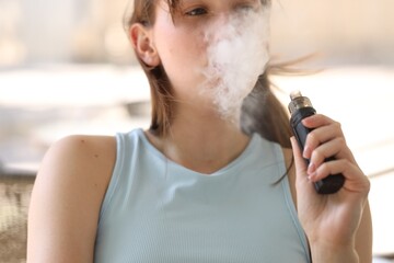 Young woman using electronic smoking device outdoors, closeup