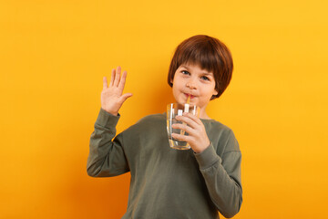 Cute little boy drinking refreshing soda on orange background