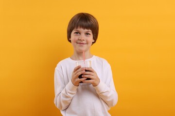 Cute little boy with glass of refreshing soda drink on orange background