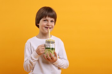 Cute little boy drinking lemonade on orange background, space for text. Refreshing drink