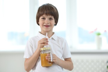 Cute little boy with mason jar of orange juice at home. Refreshing drink