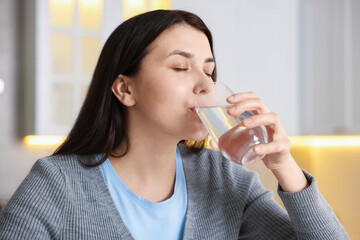 Woman drinking water from glass in kitchen
