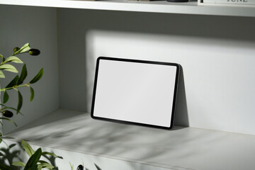 Digital tablet with blank screen on white shelf and leafy shadow