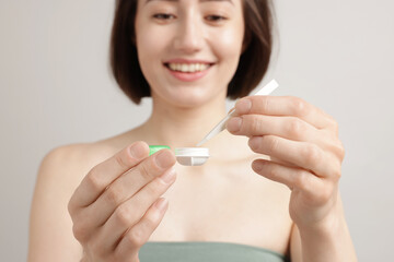Woman taking contact lens out of case on light background, selective focus