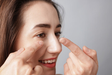 Woman putting in contact lens on light background, closeup