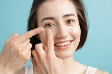 Woman putting in contact lens on light blue background, closeup