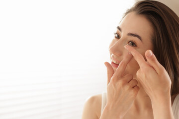 Beautiful woman putting in contact lens indoors. Space for text
