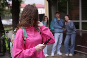 Teenage girl with smartphone suffering from bullying at school, selective focus