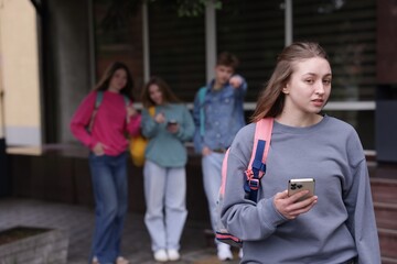 Teenage girl with smartphone suffering from bullying at school, selective focus