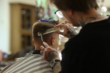 Professional barber cutting client's hair with scissors in barbershop, closeup