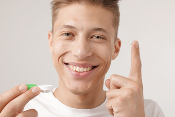 Man with contact lens and case on light background