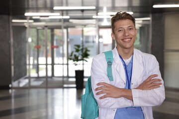 Medical student in uniform with backpack indoors, space for text