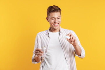 Man choosing between glasses and contact lenses on yellow background