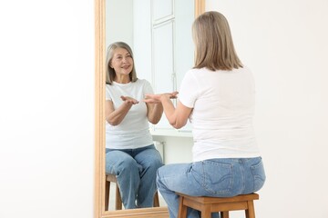 Beautiful senior woman looking at herself in mirror indoors