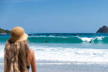 Defocused tourist watching surfers riding waves in kuta lombok, indonesia