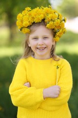 Cute little girl with beautiful flower wearing wreath of dandelions in park