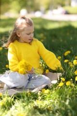 Cute little girl with beautiful dandelions on green grass outdoors