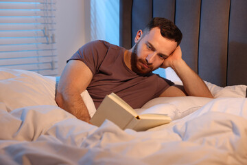 Young man reading book in bed at home