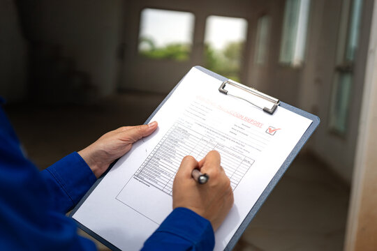 A construction foreman is checking on building quality checklist report during inspecting at the house construction site (as background). Industrial working scene, close-up with selective focus.