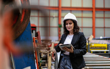 Woman engineer manager working at steel production factory. Female inspector wears safety hard hat...