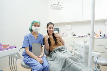 asian female dental assistant sitting beside asian female patient after treatment in dental clinic both smiling while holding digital tablet and showing clean teeth in cheerful atmosphere