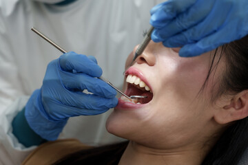 Closeup asian adult female dentist wearing gloves using dental explorer and mouth mirror checking...