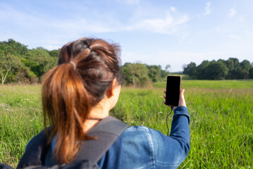 A close-up of a smartphone with a blank screen connected to a charging cable from a solar panel. Use of mobile technology and renewable energy in sustainable hiking and off-grid adventure.