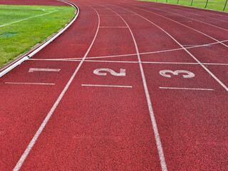 Curving red synthetic running track with lanes 1, 2, and 3, stark white markings and numbers,...