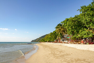 White Sand Beach on Koh Chang island with calm turquoise sea, wooden sunbeds under leaning palms,...