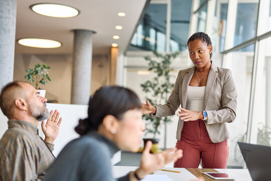 A group of businesspeople are gathered around a table, discussing something. Scene is serious and focused, as the group appears to be engaged in a discussion or decision-making process. There is a lot - Powered by Adobe