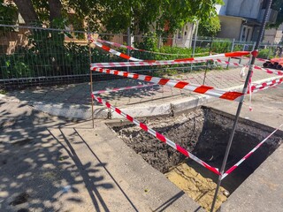A hole in the ground with a red and white striped rope around it. The rope is in the air and is...
