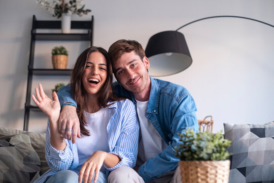 Happy young couple in a video call from home, smiling and sharing joyful news through the laptop or phone camera. Announcing engagement, vacation plans, or exciting updates with friends or family