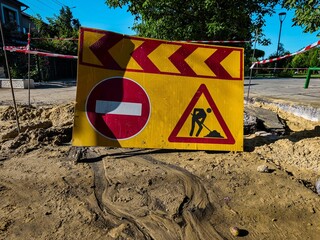 A yellow sign with a red arrow and a red circle with black lines on it. The sign is on a sandy...