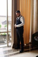 A young man in a vest and a white shirt by the window.