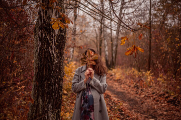 Ethereal autumn portrait of a graceful female in elegant attire, standing in a landscaped forest. A...
