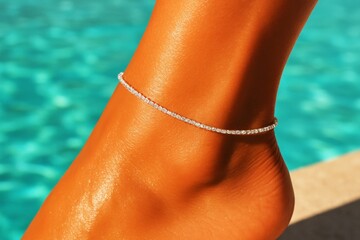 Close-up of female foot with diamond anklet against turquoise water background, summer beach jewelry and fashion concept