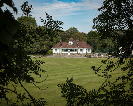  A view across a cricket pitch to the elegant red- roofed dressing rooms and pavilion in Saltaire
