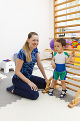 Young child is doing rehabilitation exercises near a gymnastic wall-bar to improve his movement...